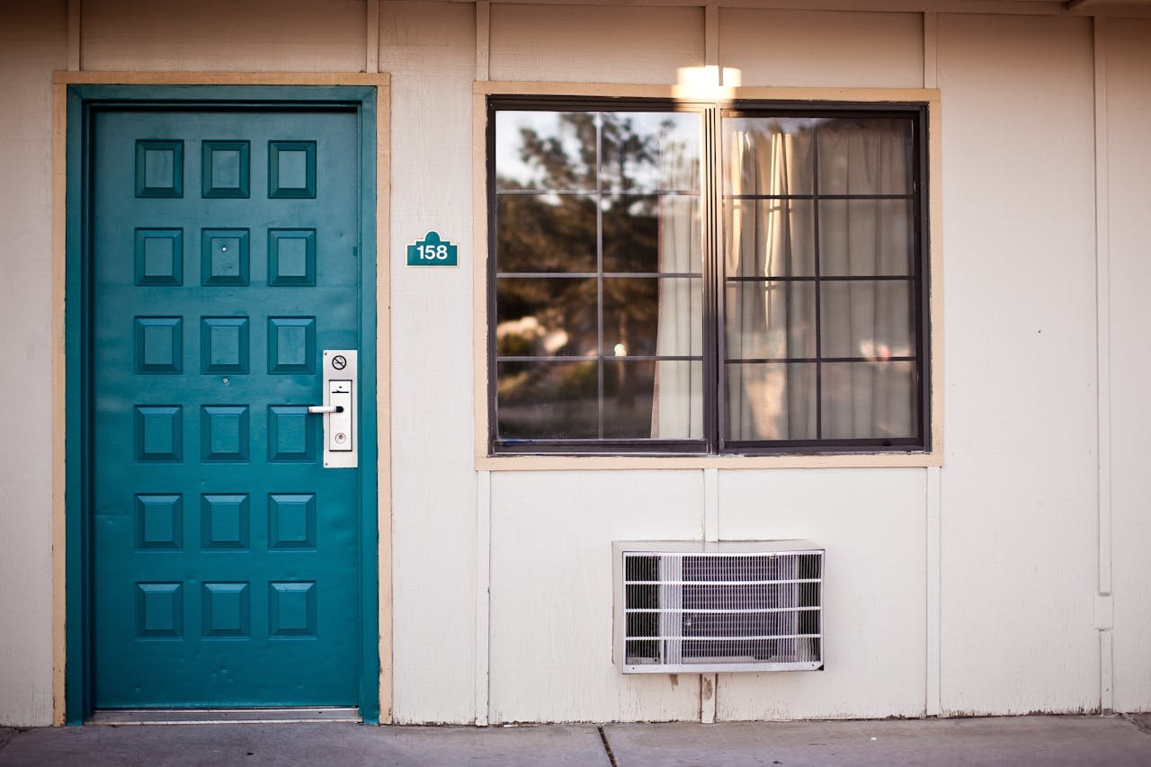 heros-img Front view of a teal door and window, typical motel exterior entrance facade.
